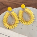 Detail of yellow raffia woven teardrop earrings with golden beads on ceramic plate - Yellow Teardrop Hollow Style (26582A)