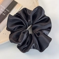 Detail of elegant black satin scrunchie with silky folds on a white dotted ceramic plate - Black
