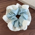 Detail van blauw-witte satijnen scrunchie met geplooide stofstructuur op houten tafel - Teal