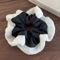 Detail van een zwart-witte geplooide satijnen scrunchie op een natuurlijk donker hout - Zwart