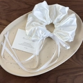Detail eines weißen Satin-Haargummis mit langen Bändern auf einem Keramiktablett - Weiß