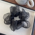 Macro shot of fluffy black organza scrunchie with layered pleated texture on white tray - Black