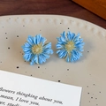 Dettaglio degli orecchini a margherita blu con petali testurizzati e centri dorati su un piatto - Fiore Blu