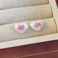 Close-up of heart pearl earrings with pink matte bows on a beige woven jewelry box - Pink Bow (26657D)