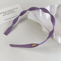 Detail van paarse gedraaide stoffen haarband met gouden ovale metalen merklogo-tag - Paarse Stijl (26678D)