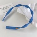 Detail van een blauwe geweven haarband met een klein goudkleurig metalen plaatje - Blauwe Stijl (26678E)