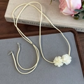 Primer plano de gargantilla de gamuza beige con flores de camelia en un escritorio de madera - Flor Beige Mate (26726B)