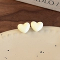 Détail de boucles d'oreilles cœur couleur crème sur un plat en céramique et décor rustique - Blanc