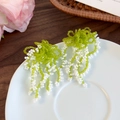 Dettaglio di orecchini a nappe con perline verdi e accenti floreali su piatto bianco - Bianco