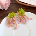 Dettaglio degli orecchini con nappe di perline rosa e verdi su un vassoio bianco - Rosa