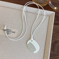 Detalle de un collar con colgante de peine blanco sobre un fondo rústico de lino color beige - Blanco