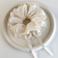 Close-up of cream lace scrunchie with floral embroidery and satin ribbons on a tray - Beige
