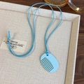 Close-up of a light blue comb-shaped pendant necklace on a beige display tray - Blue