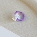 Dettaglio dell'anello di perline viola con ciondoli floreali bianchi su tessuto - Perline viola fiori bianchi (26771A)