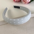 Dettaglio del cerchietto in tessuto blu con fiori bianchi ed etichetta Hand Made - Grigio