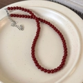 Close-up of deep red beaded necklace with silver lobster clasp on a ceramic plate - 6mm / 6mm Red Necklace