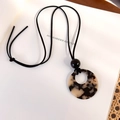 Macro detail of tortoiseshell resin pendant on a long black necklace cord over a white book - Light Tortoiseshell