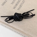 Details einer eleganten schwarzen Seidenrose Haarspange mit Satinstruktur auf Buchcover - Schwarz