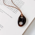 Detalle de un colgante de resina marrón en cordón negro sobre una página de libro antiguo - café