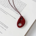 Vista de detalle de un colgante de resina rojo oscuro sobre un cordón y un libro abierto - Rojo
