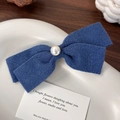 Detalle de un pasador de pelo con lazo azul y perla sobre un plato de cerámica blanca - Lazo Azul