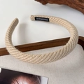 Detail of beige knit headband with wavy texture and handmade woven label on a wooden tray - Beige