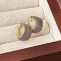 Dettaglio di orecchini a cerchio in tessuto a forma di C con perni dorati su portagioie beige - 24488F Stile Grigio