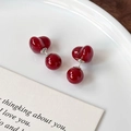 Elegante kersenrode hartbal oorknopjes op een wit keramisch bord met een kaart - Wijnrood Hartstijl