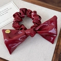 Dettaglio ravvicinato di un elastico per capelli in finta pelle bordeaux con fiocco - Rosso
