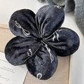Macro detail of black velvet flower hair scrunchie with white bow and dot patterns - Flower Style