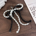 Close-up of black and white pearl bow charm with silver lobster clasp on a wooden desk - 26043J Black and Pearl Beaded Bow