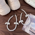 Detail view of pearl shoe chains with white bows and lobster clasps on a wooden table - 3D Bow Style (26077B)