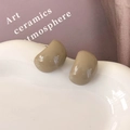 Makroaufnahme minimalistischer khakifarbener Bohnenohrringe mit Glanzfinish auf Keramik - Milchgrau