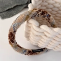 Detailopname van meerkleurige tweed hoofdband met handgemaakt label op een witte mand - Beige Koffie Meerkleurig
