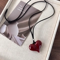 Gros plan d'un collier pendentif coeur rouge brillant sur un plateau à bijoux beige - Style de Cœur (26110A)