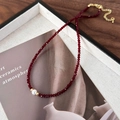 Dettaglio macro di una collana di perline rosso scuro con perla bianca e chiusura d'oro - Rosso Vino con una Perla Artificiale (26101B)