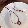 Detalle del colgante de flor roja en cordón de cera sobre un plato de cerámica - Flor Roja