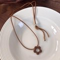 Collar con colgante de flor marrón en plato blanco sobre fondo de madera - Flor Café