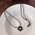 Detalle de un colgante de flor negra en un collar de cordón encerado sobre un plato de cerámica - Flor negra