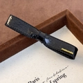 Detalle de una pinza para el pelo de cuero sintético negro con logotipo metálico minmin dorado - Negro