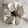 Detail shot of a beige twill fabric hair scrunchie placed on a book with soft lighting - Apricot Style