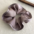 Detailed view of an elegant purple satin scrunchie on a soft textured background - Purple