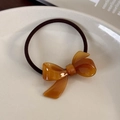 Dettaglio dell'elastico per capelli con fiocco in acetato ambra su piatto ceramico - Zucchero di Canna
