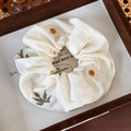 Detail van een crèmekleurige katoenen scrunchie met madeliefjes op een presentatie - Ronde Scrunchie