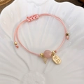 Nahaufnahme von rosa geflochtenem Armband mit Glücksanhänger und Perlen auf Schale - Rosa