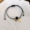 Close-up of woven bracelet with golden Zhaocai charm and beads on a shell plate - Black