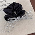 Dettaglio scrunchie in raso nero con fiocco a perline argentate su sfondo di libro - Elastico Stile Argento (25491C) / Nero
