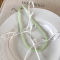 Detail of light green beaded necklace with white ribbon bows on a ceramic plate - Green Beads (25544D)