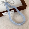 Gros plan d'un collier de perles bleu clair avec fermoir mousqueton argenté sur lin fin - Collier 10mm