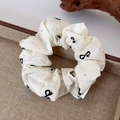 Dettaglio dello scrunchie crema con stampa a fiocco nero e rivetti in metallo - Piccolo (11cm)